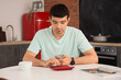 © Pixel-Shot - Young man counting money with calculator in kitchen