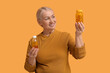 © Pixel-Shot - Mature woman with bottle of pills and bottle of fish oil on orange background