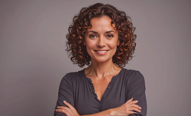 Poster - Woman with curly hair is smiling and posing for a picture. She is wearing a black shirt and has her arms crossed