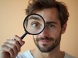 © Michael - Young man showing his eye through magnifying glass on orange background