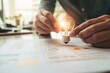 © Anjali - A person holds a glowing lightbulb above business documents, symbolizing a brilliant idea or innovative solution.