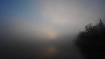 Wall Mural - Spooky calm misty morning at a still lake as fog moves above the water. Trees on side.
