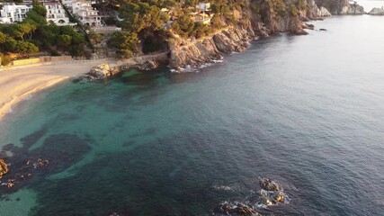 Wall Mural - Aerial view of a peaceful beach with clear blue waters and rocky coastline. Green trees and white houses line the shore, creating a serene getaway for relaxation and fun.
