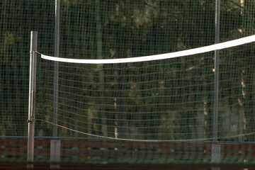 a volleyball net is enclosed by a sturdy fence, while trees beautifully line the background creating