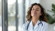 © Choose Me - A female doctor with wavy brown hair, wearing a white coat and stethoscope, stands with her eyes closed and a serene expression on her face.