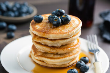 Wall Mural - Pancakes with blueberries stack on white ceramic plate served with maple syrup, closeup view, vertical