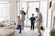 © fizkes - Happy Indian couple and their cute little kids dancing together, moving to favourite music in stylish living room of high-rise apartment with views of city skyline. Family activity, pastime and fun
