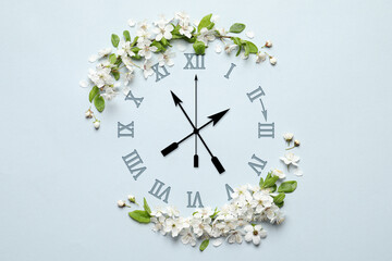 Poster - Clock and white flowers on light blue background, top view. Arrow showing time change one hour ahead in spring. Daylight saving time