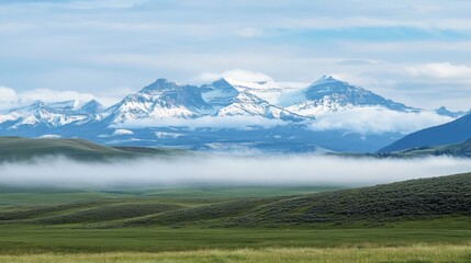 Leinwandbilder - Majestic snow capped mountains rise above misty valleys and green hills on a clear day in the wilderness