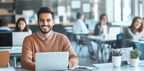 Poster - A young, smiling professional sits at a modern workspace, confidently using a laptop. The bright office background features colleagues engaged in teamwork and productivity.