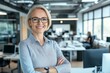 © Tondone - A confident businesswoman stands in a modern office, smiling and crossing her arms
