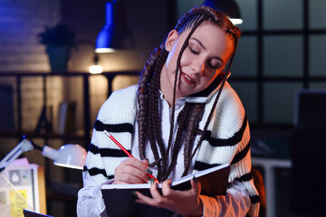 Fototapete - Female designer with notebook talking by mobile phone in office at night