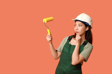 Wall Mural - female asian thoughtful painter with roller on orange background