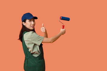 Wall Mural - female asian painter with roller showing thumb-up gesture on orange background