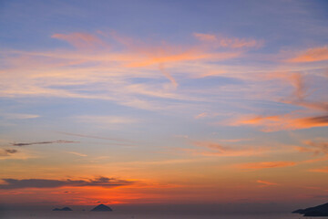 Wall Mural - Cirrus evening clouds backlit by the sun, gradien orange blue sky view over the sea with islands horizon