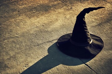 Wall Mural - A black hat with a pointed top is sitting on a concrete floor. The hat casts a shadow on the ground