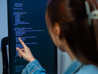 focused asian female software developer writing code on laptop computer working in office. professio