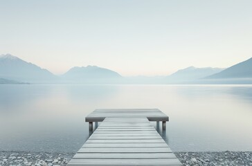  Serene lake view with a wooden dock extending into calm waters, surrounded by mountains under a gentle, overcast sky.