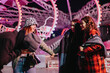 © qunica.com - A group of friends sharing laughter and joy under the colorful lights of an amusement park at night, showcasing a spirit of friendship and fun-filled adventure in a vibrant setting.