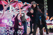 © qunica.com - A joyful group of friends celebrating and enjoying themselves at a colorful carnival, featuring bright lights, festive decorations, and playful moments.