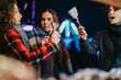 © qunica.com - Three friends share laughter and lollipops under colorful lights during a winter celebration.
