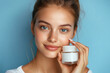 © Mariant - A young woman enjoys her pampering beauty routine while holding a jar of cream, showcasing radiant skin and a joyful expression