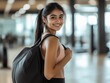 © Eman Suardi - A smiling young woman in athletic wear with a backpack in a gym setting.