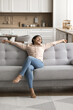© fizkes - My sweet homey. Vertical shot smiling millennial female take break relax on comfortable sofa at cozy domestic interior spread arms wide enjoy weekend at home feel happy being homeowner renter tenant