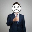 © Metehan - Businessman covering face with a sad face drawing and giving a thumbs up, conveying mixed feelings or hidden emotions.