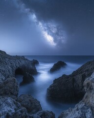 Wall Mural - majestic milky way galaxy illuminates a tranquil coastal seascape with rugged rocks and smooth water