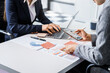 © Phushutter - Two female business professionals in suits sit at desk, engaged in strategic discussion. They analyze financial planning, risk management, corporate growth while reviewing reports and market trends.