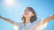 © bephoto - 青空の下で両手を広げる笑顔の女性