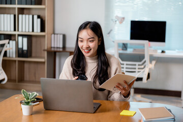 Poster - Professional Asian female working remotely, videoconferencing with laptop, notebook, and coffee mug in contemporary workspace