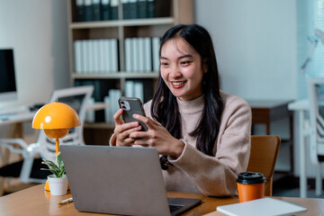 Poster - Happy businesswoman typing on mobile phone and looking at screen while working on laptop in modern office