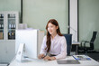 © laddawan - Asian woman, smiling and working at her desk in an office environment. She is wearing a business suit and holding documents