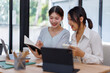 © David - Happy professional young women collaborating with enthusiasm in a modern office setting. Two asian female entrepreneurs using a laptop for a productive business meeting in a corporate workplace.