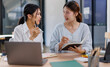 © David - Happy professional young women collaborating with enthusiasm in a modern office setting. Two asian female entrepreneurs using a laptop for a productive business meeting in a corporate workplace.