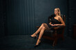 © Jurii - Elegant young girl in black dress sitting in vintage leather chair, radiating confidence and sophistication. Stylish portrait with dark moody background