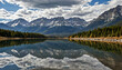 © SolarisKG - Le reflet du ciel dans un lac de montagne entouré d'arbres et de montagnes enneigées.