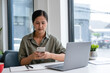 © MIND AND I - Businesswoman sitting at desk on couch in workplace or at home working on laptop and analyzing data on charts and graphs and writing on papers to make business plan and strategies for company,