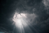 Rays of light through the hole in the dark stormy clouds in the sky.