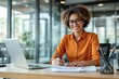 © PlanetOfVectors - Smiling woman in orange shirt writing at desk with laptop, creative office background. Professional and success concept. Ai generative