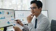 © Qbertstudio - Asian man in business attire reviews data analysis reports in a modern office workspace, focusing on productivity and career development