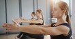© procinemastock - Woman stretching and resting during group pilates workout. Glad female bending forward and stretching back then breathing and turning head to camera against women doing pilates exercise during