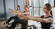 © procinemastock - Woman exercising during group pilates training. Tracking shot of fit female lifting body and stretching leg then tilting back on reformer during group pilates workout in gym