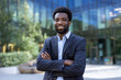 © Liubomir - Portrait of successful confident businessman. Man in business suit smiling and looking at camera. African American company employee outside office building with arms crossed.
