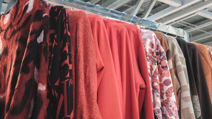 Poster - A rack of clothes with a variety of colors and patterns. The clothes are hanging on a rack, and the colors include red, orange, and brown. Scene is vibrant and lively