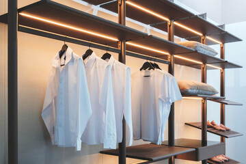 Aufkleber - A closet with clothes hanging on the racks. The clothes are white and the racks are black. The closet is lit up