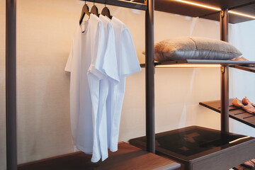 Aufkleber - A closet with clothes hanging on the racks. The clothes are white and the racks are black. The closet is lit up