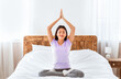 © Prostock-studio - Relaxed Korean Woman Doing Yoga Meditating Sitting In Lotus Pose On Bed At Home. Meditation Concept